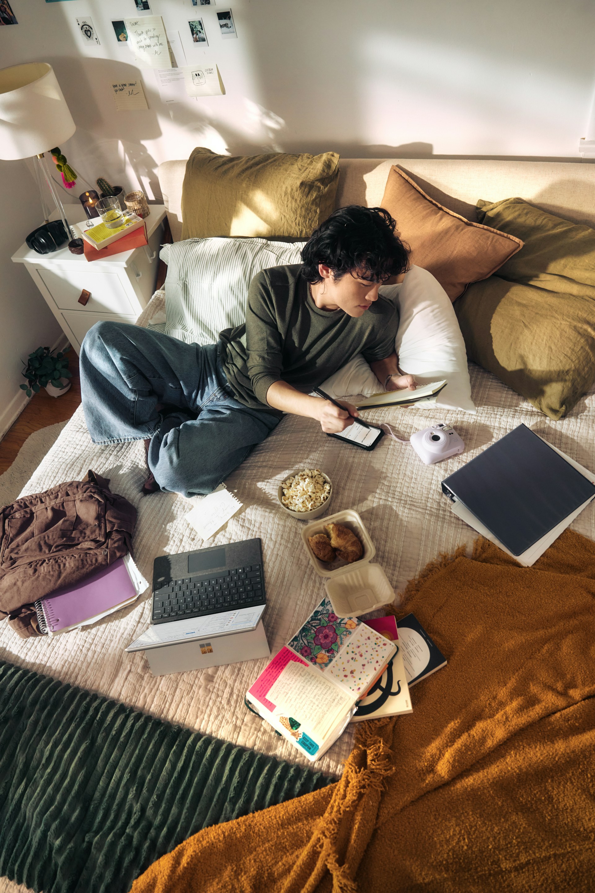 A university student sitting on a bed studying with a laptop and notebooks, representing the students eligible for the MenB catch-up vaccine